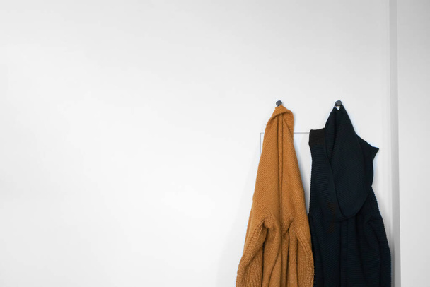 Black and yellow cardigans on hangers against the background of white wall. Autumn warm clothing - Photo, Image