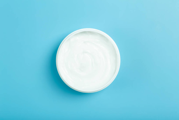 Cosmetic cream background. White cosmetic cream for skin and body in an open white jar on a colored blue empty background. - Foto, Bild