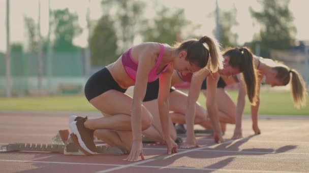Três jovens mulheres no estádio na linha de partida em blocos começam na corrida em câmera lenta - Filmagem, Vídeo