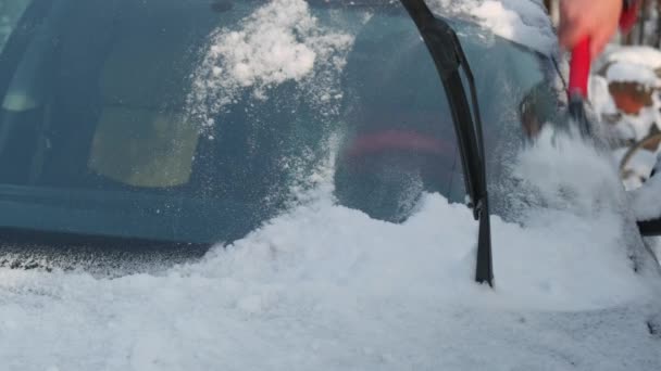 Een man ruimt de sneeuw uit de auto. Man ruimt sneeuw uit zijn auto op straat in de winter - Video