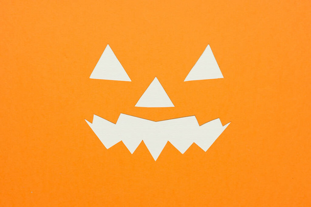 Halloween-Hintergrundkonzept mit Schichten aus orangefarbenem und weißem Papier in Form eines Jack O Lantern-Gesichts und Papierkunstwerken eines gruseligen Gesichts eines Halloween-Kürbisses. - Foto, Bild