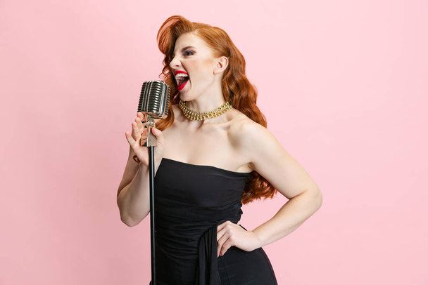 Portrait en studio recadré d'une belle chanteuse expressive sur scène donnant une performance isolée sur fond rose. - Photo, image