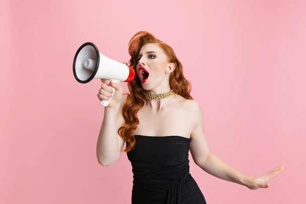 Cropped portrait of beautiful woman with retro hairstyle singing in megaphone isolated over pink background - Photo, Image