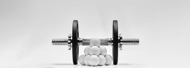白い背景にダンベルと鉄の重みを持つゴルフボール。より強い力のためのトレーニングコンセプト. - 写真・画像
