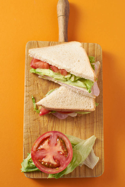 Υγιεινό σάντουιτς με ζαμπόν και τυρί με ντομάτα και μαρούλι σε πορτοκαλί φόντο - Φωτογραφία, εικόνα