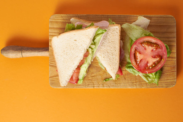 Turuncu arka planda domates ve marullu sağlıklı jambonlu ve peynirli sandviç. - Fotoğraf, Görsel