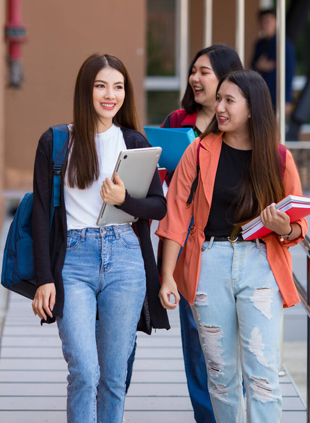 Company of cheerful Asian female students with notebooks walking in university campus and taking togeter with fun and intimate feeling. Close friend in college concept. - Photo, Image