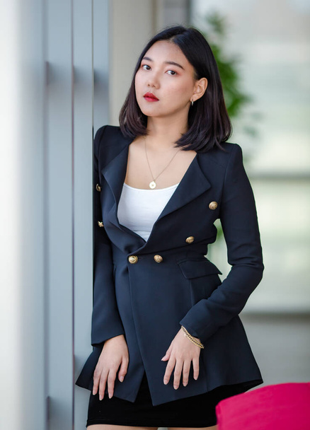 Entschlossene asiatische Unternehmerin im eleganten Outfit steht neben Fenstern im Büroflur und blickt in die Kamera - Foto, Bild