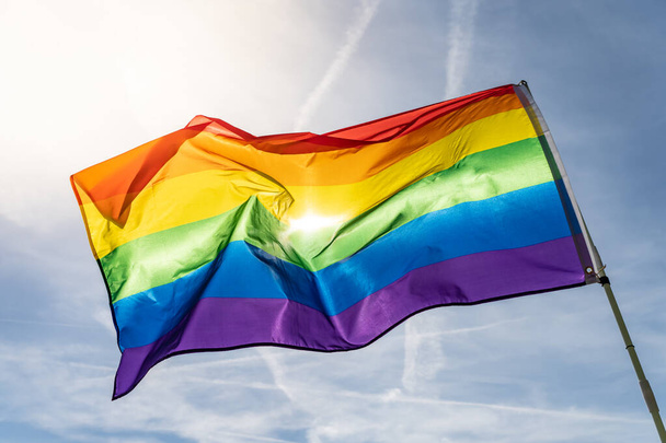 Rainbow flag (LGBT movement) on the sunny blue sky background. Colorful gay flag waving. - Foto, Bild