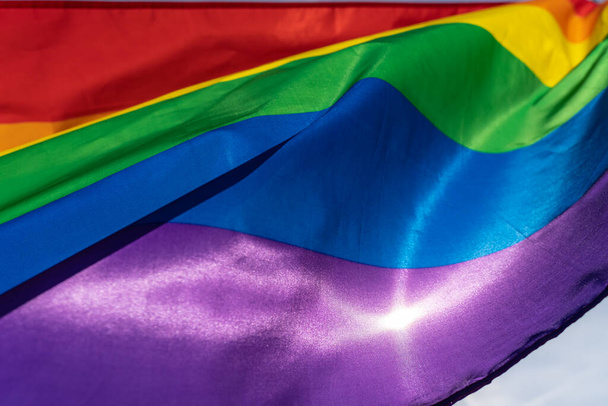 Rainbow flag (LGBT movement) on the sunny blue sky background. Colorful gay flag waving. - Fotó, kép