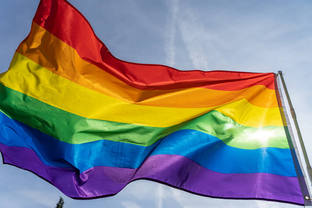 Rainbow flag (LGBT movement) on the sunny blue sky background. Colorful gay flag waving. - 写真・画像