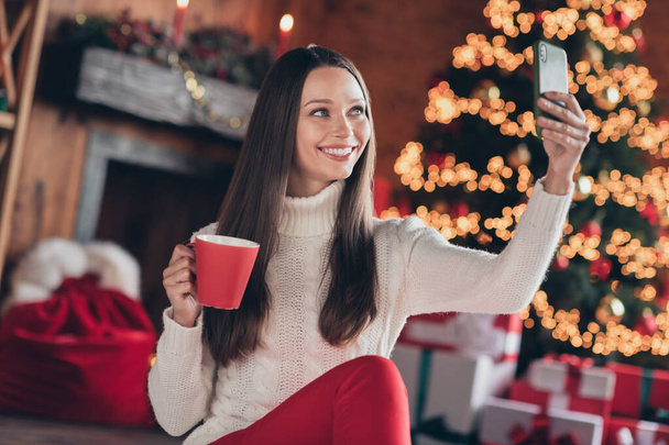 Photo of charming pretty young woman dressed knitted sweater drinking beverage tacking selfie smiling indoors room home house - Photo, image