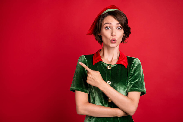 Photo of amazed shocked woman santa helper elf point finger empty space sale holiday isolated on red color background - Fotografie, Obrázek
