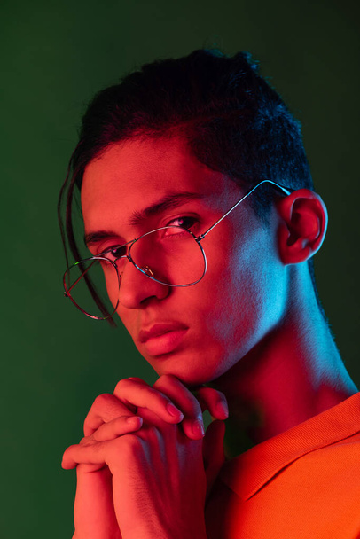 Close-up portrait of young man, student posing isolated on green studio backgroud in neon light. Human emotions concept. - Фото, зображення