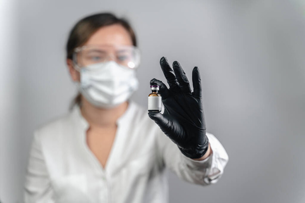 Zbliżenie ręki lekarza trzymającego Butelkę ze szczepionkami używaną do leczenia lub badania, badania kliniczne nad wirusem Covid-19 lub korony w biurze, badanie szczepionki, która skutecznie wyleczyła wirusa - Zdjęcie, obraz