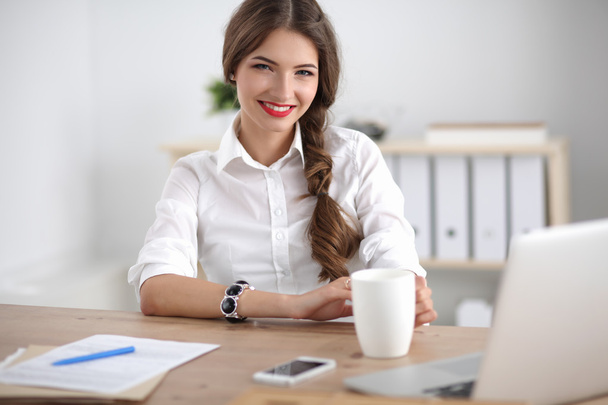 Young businesswoman sitting on the desk with cup in office - Valokuva, kuva