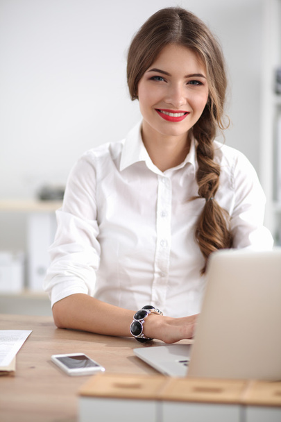Attractive businesswoman sitting  on desk in the office - 写真・画像