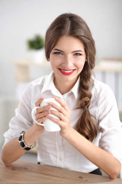 Young businesswoman sitting on the desk with cup in office - Foto, Bild