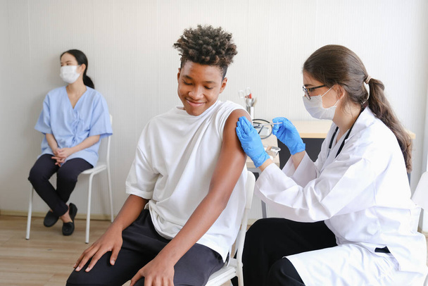 Médico caucásico mujer o enfermera que da gripe o vacuna antiviral al hombre afroamericano en el hospital o clínica - Foto, Imagen