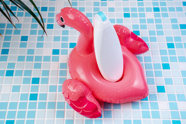 Shampoo on a background of blue tiles. Shower gel in a flamingo inflatable ring. Vacation cosmetics. Mockup Shower gel in the lifebuoy. - Photo, Image