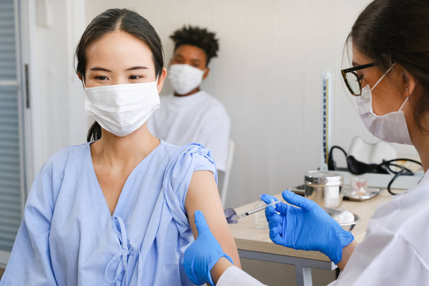 Blanke arts vrouw of verpleegkundige die griep of antiviraal vaccin geeft aan Aziatische vrouw in ziekenhuis of kliniek - Foto, afbeelding