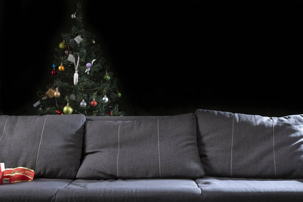 Sofa against the background of the Christmas tree. Christmas Eve. Black background. - Foto, Imagen