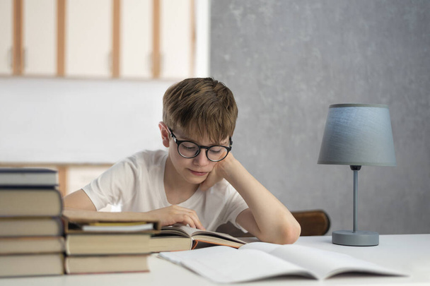 Lo studente con gli occhiali fa i compiti. Imparare a distanza. Il ragazzo legge un libro di testo. Istruzione a domicilio. - Foto, immagini