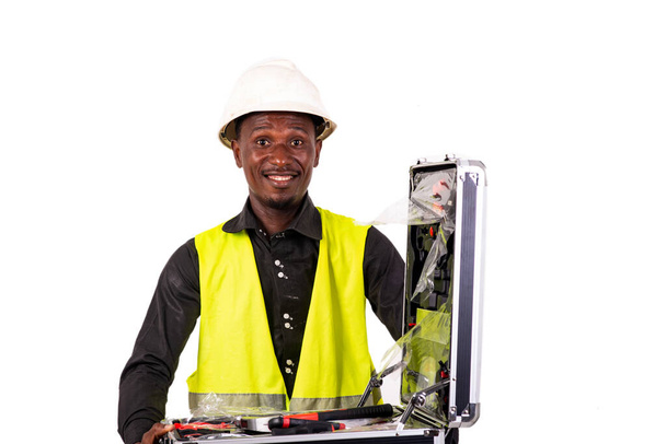 ツールボックスの笑顔を保持しながら緑のベストと安全ヘルメットを身に着けている若い男性技術者. - 写真・画像