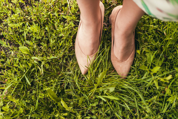 Female legs in beige suede shoes on a green grass field. View from above - Photo, Image
