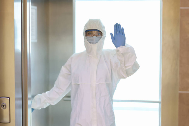 Nő védőruhában és orvosi maszkban kesztyűben áll a liftben - Fotó, kép