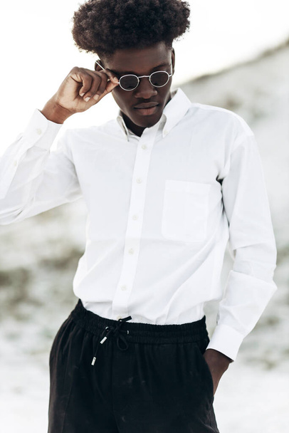 Handsome fashionable african american hipster man, in stylish sunglasses and in a white shirt, posing on the street, fashion posing, fashion, style - Zdjęcie, obraz