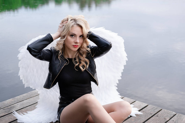 Pimeä enkeli blondi seksikäs nainen musta nahka vaatteet valkoinen enkelit siivet. - Valokuva, kuva