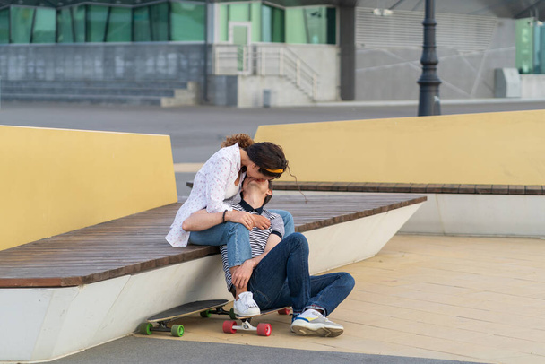 Un par de patinadores besándose se sientan en longboard juntos al aire libre en el espacio urbano. Juventud, romance y amor - Foto, Imagen