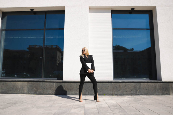A young woman in a stylish suit with a laptop poses against the background of a business center - Фото, зображення