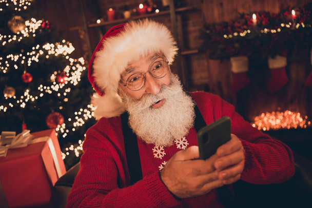 Foto di divertente eccitata età Babbo Natale indossare costume rosso digitando dispositivo moderno sorridente all'interno della stanza della casa - Foto, immagini