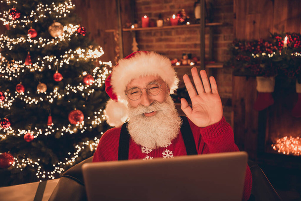 Photo of friendly pretty age santa claus wear red costume talking modern gadget waving arm indoors house room - Foto, immagini