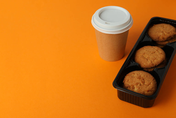 Cookies και χάρτινο φλιτζάνι καφέ σε πορτοκαλί φόντο. - Φωτογραφία, εικόνα