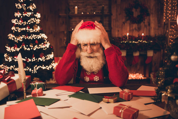 Photo of troubled overwhelmed santa claus sit workspace delivery service wear hat sweater in north pole office indoors - 写真・画像