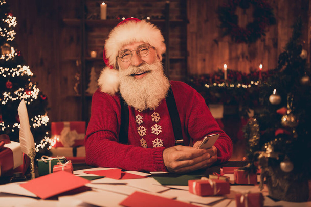 Photo of aged cheerful santa claus happy positive smile use smartphone sit desk north pole christmas time decor indoors - Fotoğraf, Görsel