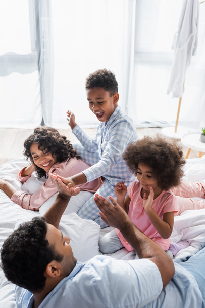 african american man playing patty cake game with kids in bed near cheerful wife - Photo, Image