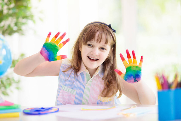 Kind zeichnet Regenbogen. Farbe auf die Hände. Fernlernen und Online-Schulkunstaufgaben von zu Hause aus. Basteln für Kinder. Kleines Mädchen zeichnet ein helles Bild. Kreative Kinder spielen und lernen. - Foto, Bild