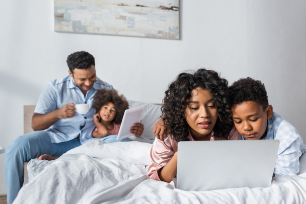 афроамериканські батьки з дітьми використовують ноутбук і цифровий планшет у спальні
 - Фото, зображення