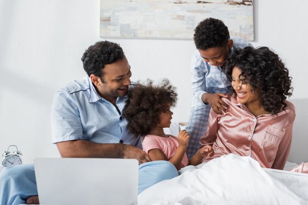 african american man near laptop and cheerful family in bedroom - Foto, imagen