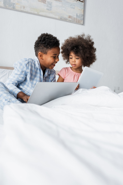 african american siblings using laptop and digital tablet in bed - 写真・画像