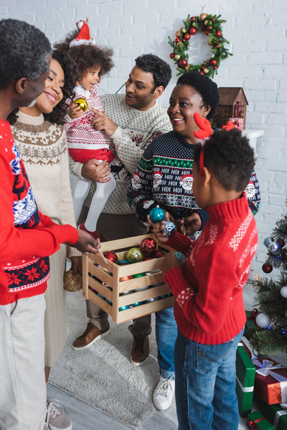 joyful african american family choosing christmas balls from wooden box at home - Foto, imagen