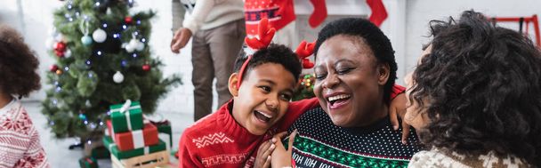 heureux garçon et femme étreignant rire afro-américaine mamie près floue famille et arbre de Noël, bannière - Photo, image