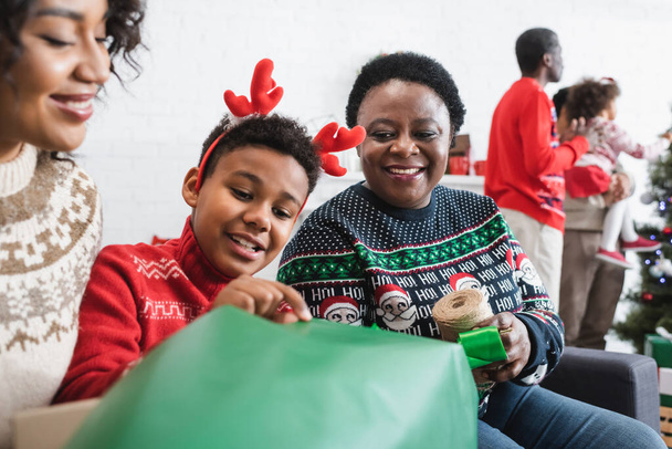 afro-américain garçon en cornes de renne bandeau emballage cadeau de Noël avec mère heureuse et mamie - Photo, image