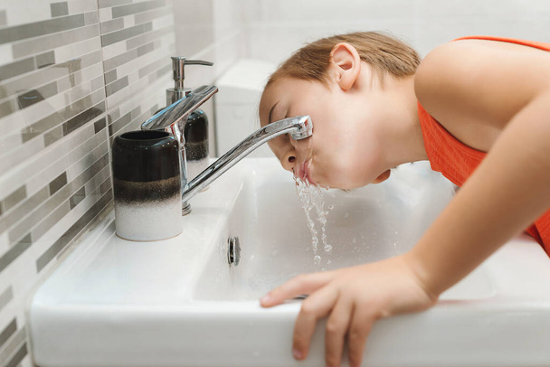 Το παιδί πλένει το πρόσωπο του στο μπάνιο. Πρωινή υγιεινή. Ο έφηβος πλένεται σε νιπτήρα. Υγιής παιδική ηλικία και τρόπος ζωής. Υγιεινή των δοντιών κάθε μέρα. Υγειονομική περίθαλψη, παιδική και οδοντιατρική υγιεινή. - Φωτογραφία, εικόνα