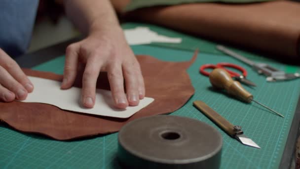 Trabajador de taller aplicando plantilla a la pieza de cuero en la alfombra de escala interior - Imágenes, Vídeo