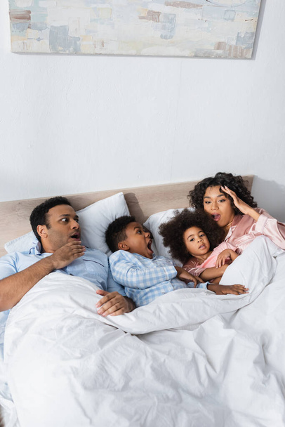overslept and shocked african american couple lying with kids in bed - Foto, imagen